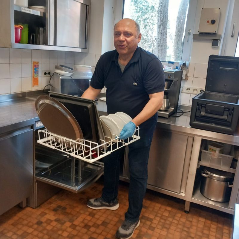 Hossein füllt die Spülmaschine in der Küche.